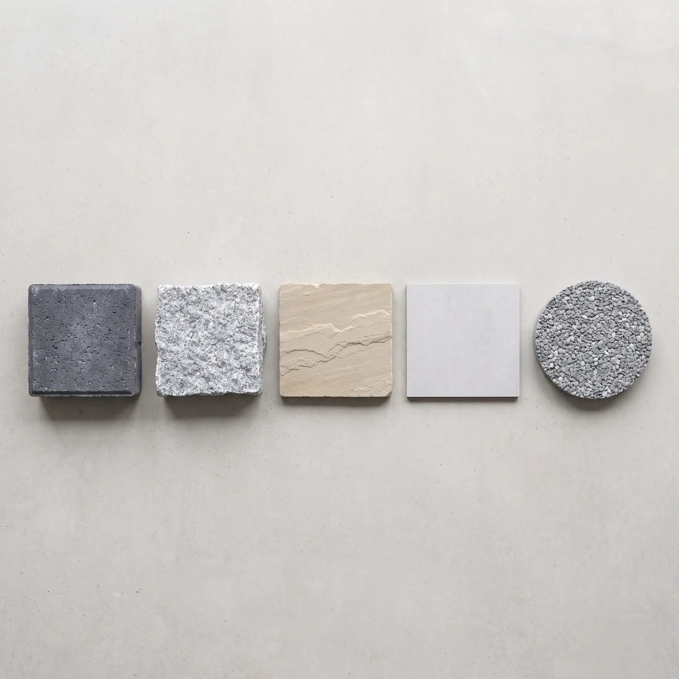 Five paving samples in a row: charcoal block, granite sett, buff sandstone, grey porcelain and resin aggregate